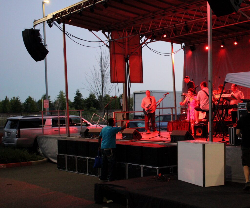 Band on an outdoor stage under red light at dusk